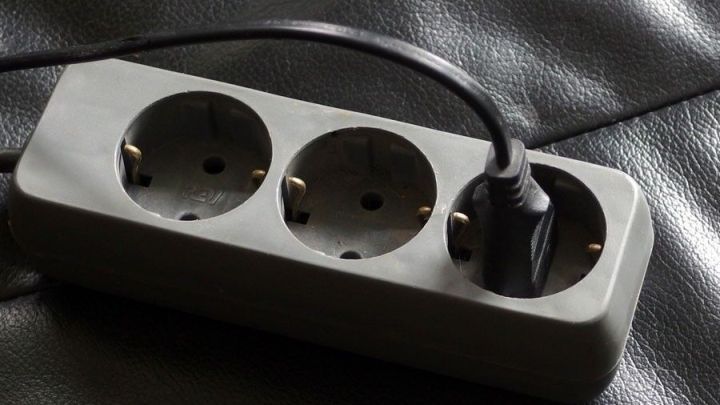 Eine mehrfach Steckdose liegt auf einem dunklen Untergrund und hat ein Kabel angeschlossen, um Strom zu sparen.