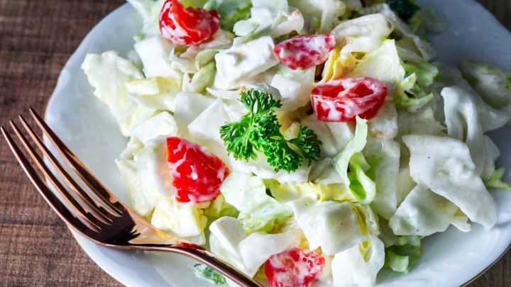 Eine Sch&uuml;ssel frischer Salat mit Sahne-Gartenkr&auml;uter-Dressing, garniert mit Tomaten und Petersilie, auf einem Holztisch.