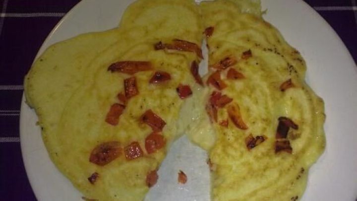 Zwei Eierpfannkuchen mit St&uuml;cken von Raclettek&auml;se liegen auf einem wei&szlig;en Teller, umgeben von einem dunklen Tischdeck.