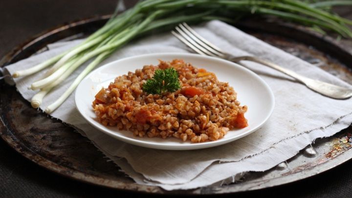 Zarte Buchweizengr&uuml;tze liegt auf einem wei&szlig;en Teller, garniert mit frischem Schnittlauch, auf einem rustikalen Tablett.
