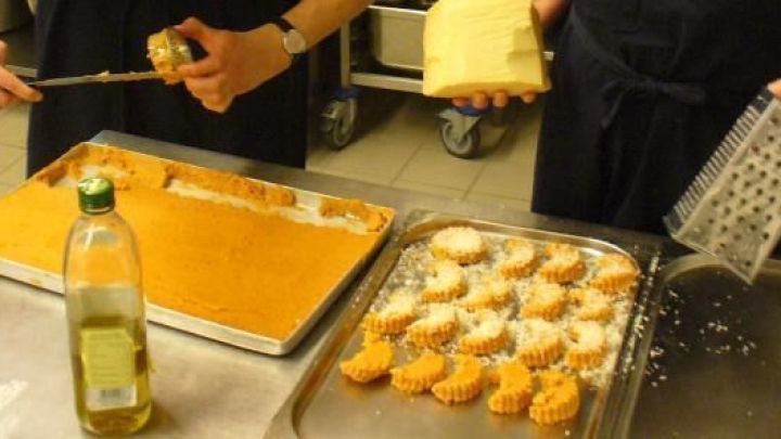 K&ouml;che schneiden Tomatenpolenta aus einem Blech und reiben K&auml;se dar&uuml;ber, in einer professionellen K&uuml;chenumgebung.