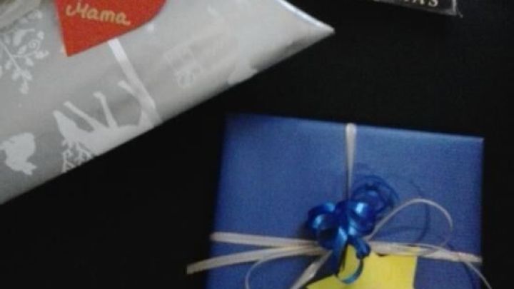 Ein blauer Pr&auml;sentkarton mit gelbem Geschenkanh&auml;nger liegt neben der Dekoration und einem weiteren verpackten Geschenk.