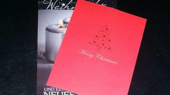 Ein roter Geschenkanh&auml;nger aus einer alten Weihnachtskarte liegt auf einem schwarzen Untergrund neben einer weiteren Karte und strahlt festliche Stimmung aus.