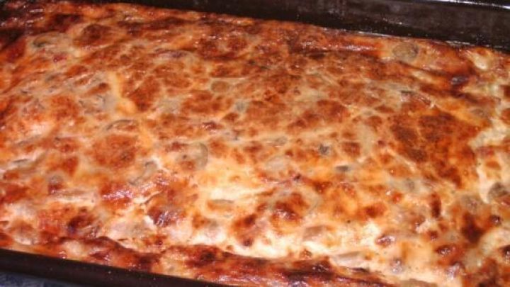 Eine gebackene Quiche ohne Teig liegt in einer schwarzen Backform auf einem blauen Tuch, frisch gebr&auml;unt und servierbereit.