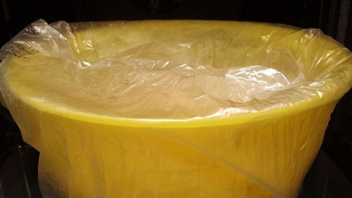 Ein gelber Beh&auml;lter mit Hefeteig ist mit Plastikfolie abgedeckt und wartet darauf, zu gehen, in einer hellen K&uuml;che.