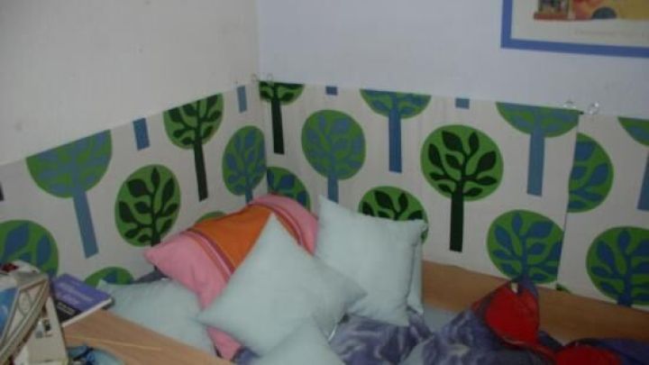 Selbstgemachte Bettumrandung aus Kissen in einem bunten, mit Baummotiven dekorierten Kinderzimmer-Eckbereich.