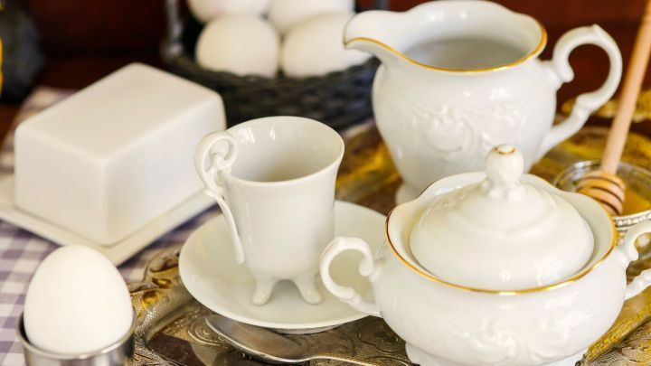 Eine wei&szlig;e Teekanne und Tasse stehen auf einem Tablett, w&auml;hrend ein Ei und Butter daneben bereit f&uuml;r ein schnelles Fr&uuml;hst&uuml;ck sind.