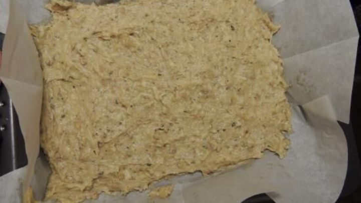 Ein flacher Teigblock aus Leberwurst und Kartoffeln liegt auf Backpapier in einer Form und wartet auf das Backen.