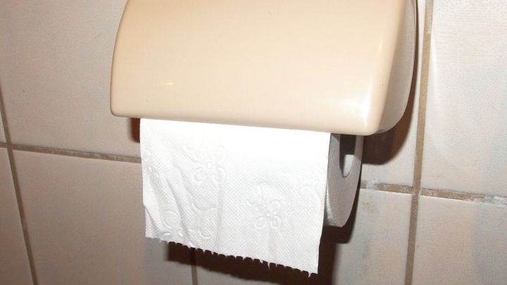 Ein Toilettenpapierhalter mit frischem, gefaltetem Toilettenpapier h&auml;ngt an einer gefliesten Wand und bietet Hygiene zur Verstopfung reduzieren.