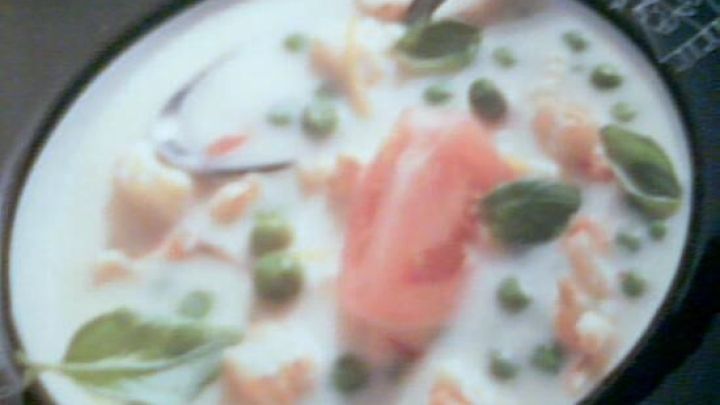 Eine cremige Suppe in einer schwarzen Schale, mit L&ouml;ffel, enthaltend Erbsen, Lachsst&uuml;cke und Basilikumbl&auml;tter.