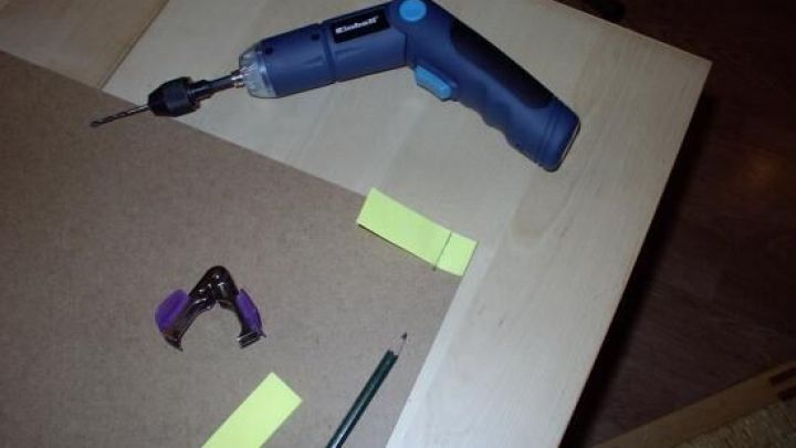 Ein Akku-Bohrer liegt auf einer Holzplatte, umgeben von Werkzeug und Markierungen f&uuml;r gleichm&auml;&szlig;ige Abst&auml;nde beim Heimwerken.