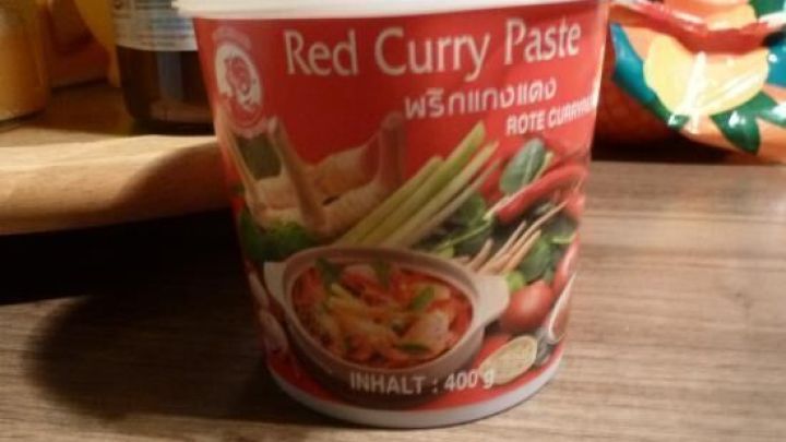 Ein Beh&auml;lter mit roter Currypaste steht auf einem Holztisch, umgeben von frischen Zutaten f&uuml;r einen asiatischen Fischtopf.