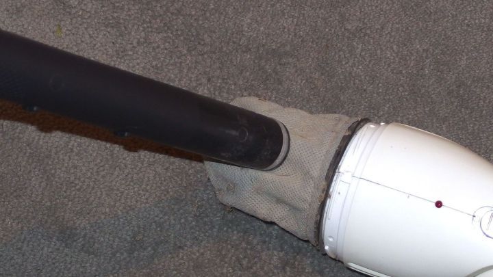 Ein Handstaubsauger steht auf einem Teppich und wird gerade entleert, w&auml;hrend sich der Schmutz l&ouml;st.