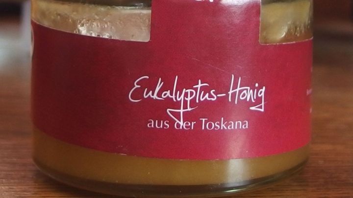 Ein Glas Eucalyptus-Honig steht auf einem Holztisch, umgeben von einer gem&uuml;tlichen Innenraumatmosph&auml;re.