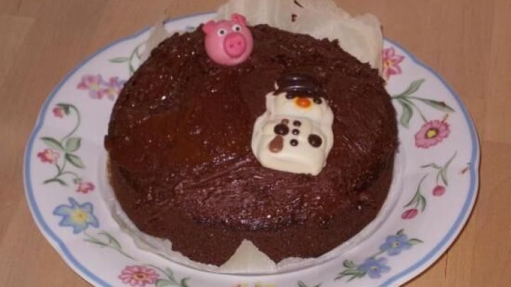 Eine kleine Erdnuss-Schokoladen-Torte steht auf einem blumengeschm&uuml;ckten Teller, dekoriert mit bunten Figuren.