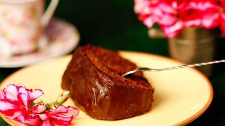 Saftiger Schokokuchen liegt auf einem gelben Teller, w&auml;hrend eine Gabel bereit ist, ein St&uuml;ck zu nehmen, umgeben von Blumen.