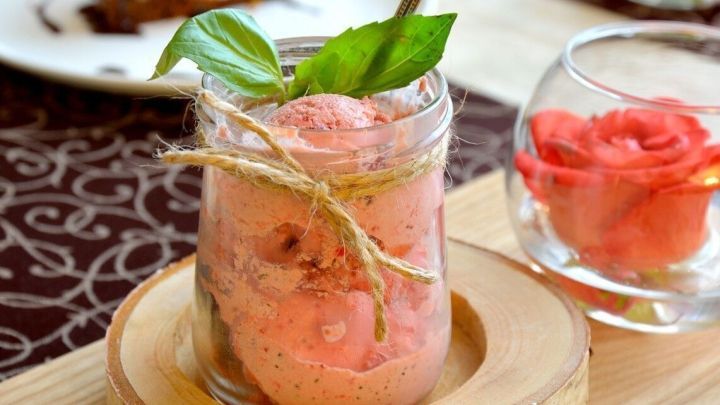 Ein Glas selbstgemachtes Erdbeereis steht auf einem Holzbrett, umgeben von einem eleganten Tischgedeck in einem gem&uuml;tlichen Ambiente.