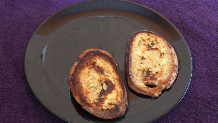 Zwei goldene Brotscheiben liegen auf einem schwarzen Teller und zeigen eine krosse, gebr&auml;unte Oberfl&auml;che auf lila Tischdecke.