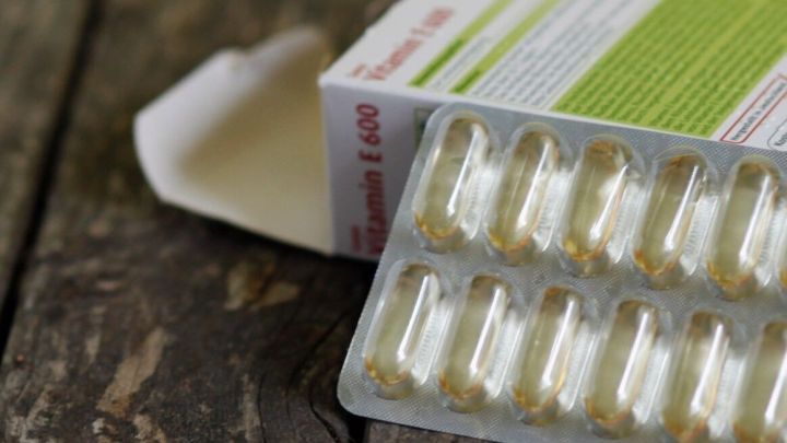Eine Blisterpackung mit Vitamin E-Kapseln liegt auf einem rustikalen Holztisch, suggeriert die Einnahme gegen Warzen.