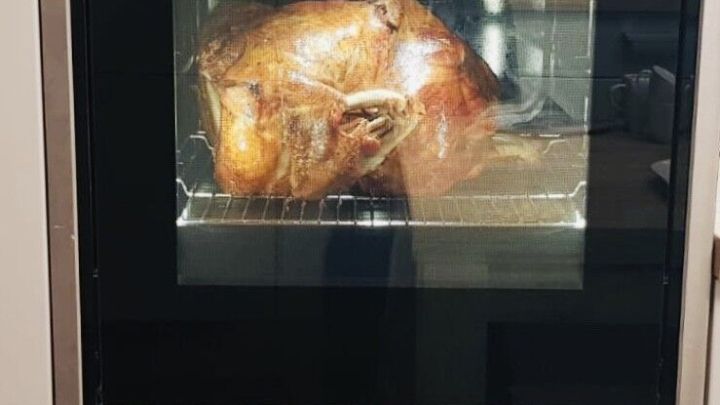 Ein Backofen zeigt ein goldbraun gebratenes H&auml;hnchen. Es befindet sich in einer modernen K&uuml;che und gl&uuml;ht leicht.