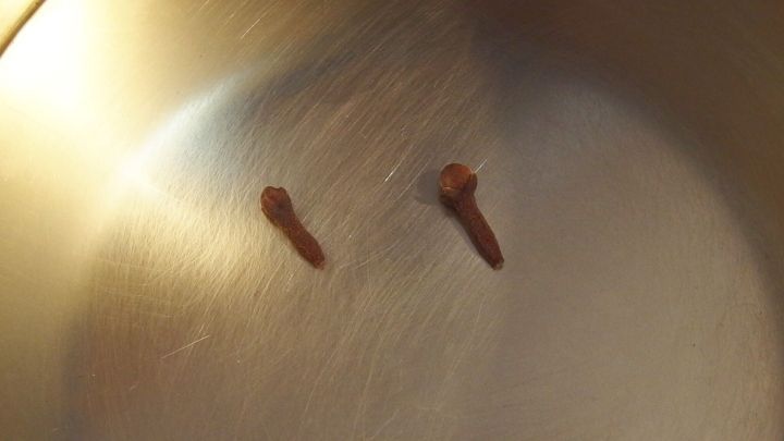 Zwei Gew&uuml;rznelken liegen auf der gl&auml;nzenden, metallischen Oberfl&auml;che eines Kochtopfs, bereit zur Beseitigung von Ger&uuml;chen.