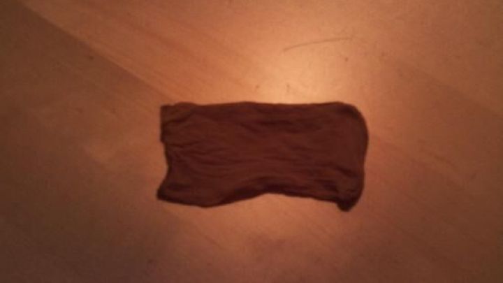 Ein brauner Stoffrest liegt auf einem hellen Boden, beleuchtet von einem warmen Licht, das eine gem&uuml;tliche Atmosph&auml;re schafft.