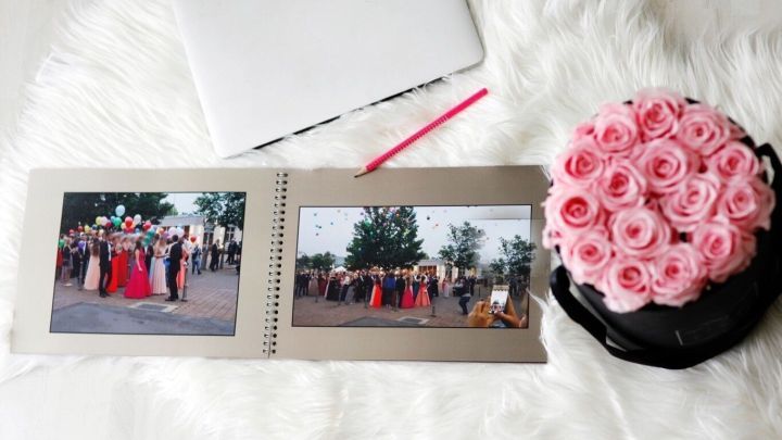 Ein Fotoalbum mit Bildern von einer Veranstaltung liegt auf einem weichen Untergrund, daneben eine Blume und ein Laptop.