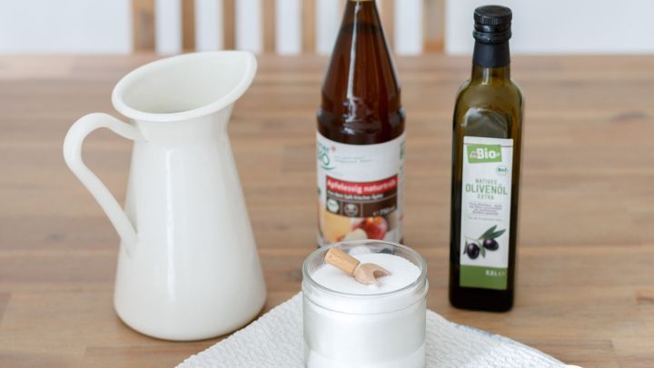 Ein Krug, eine Flasche Apfelessig naturtr&uuml;b, eine Bio-Oliven&ouml;lflasche und ein Glas Salz mit L&ouml;ffel stehen auf einem Tisch.