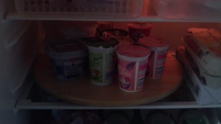 Im K&uuml;hlschrank befinden sich mehrere Joghurtbecher auf einem Holztablett, umgeben von anderen Lebensmitteln.