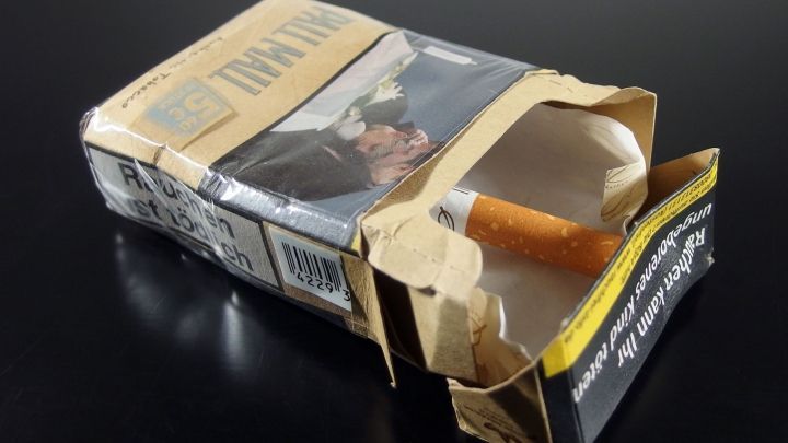 Eine ge&ouml;ffnete Zigarettenschachtel liegt auf einem schwarzen Tisch, eine Zigarette ragt heraus, was den Verzicht symbolisiert.