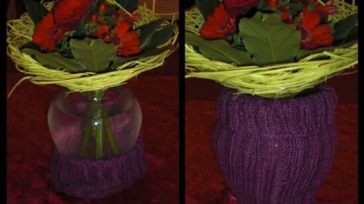 Eine bauchige Vase, umwickelt mit lila Stulpen, h&auml;lt einen bunten Blumenstrau&szlig; und steht auf einem roten Untergrund.