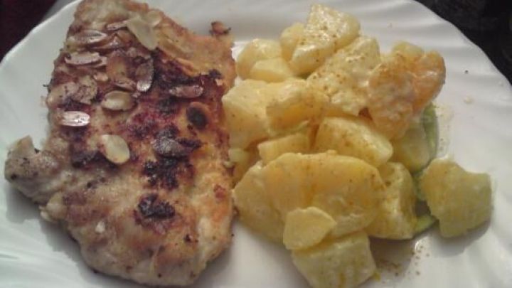 Ein knuspriges Mandelschnitzel liegt auf einem wei&szlig;en Teller, umgeben von frischem indischem Kartoffelsalat.