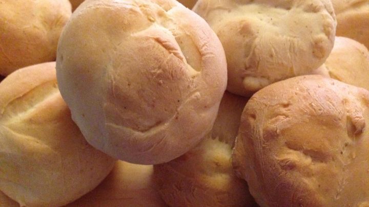 Auf einem Holzbrett liegen frisch gebackene Br&ouml;tchen, die goldbraun und fluffig sind, bereit zum Servieren.