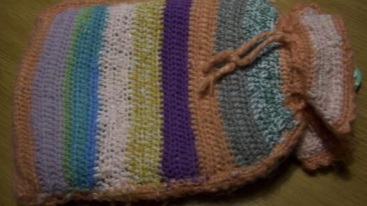 Ein gestreifter Bezug f&uuml;r die W&auml;rmflasche liegt auf einem Holztisch und bietet W&auml;rme und Komfort im k&uuml;hlen Raum.