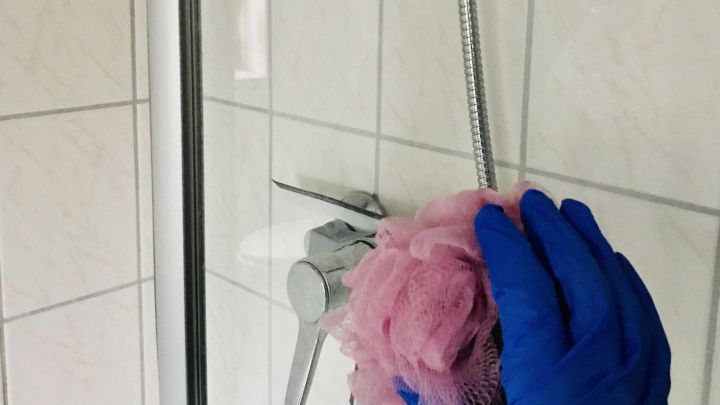 Ein alter Duschschwamm wird in einer Dusche verwendet, um die Fliesen gr&uuml;ndlich zu reinigen.