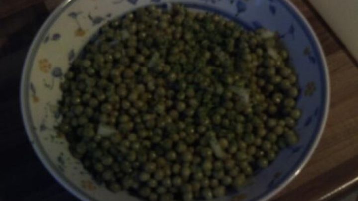 Ein dekorativer Teller Erbsensalat steht fertig angerichtet auf einem Holztisch, bereit zum Servieren.