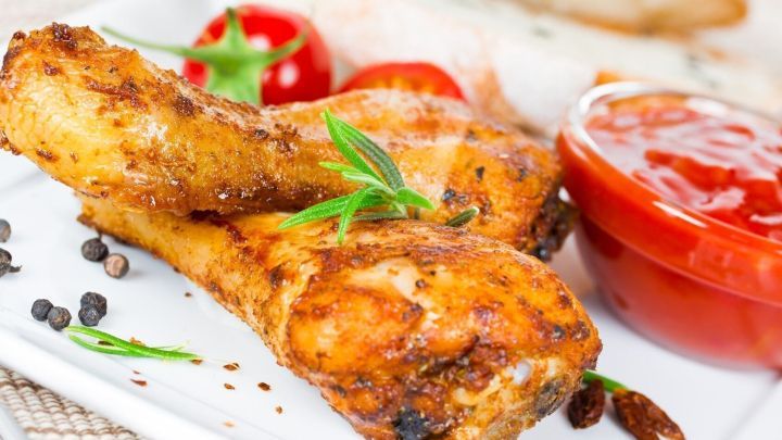 Saftiges Grillh&auml;hnchen mit knuspriger Haut liegt auf einem Teller, umgeben von Tomaten und einer Sauce.