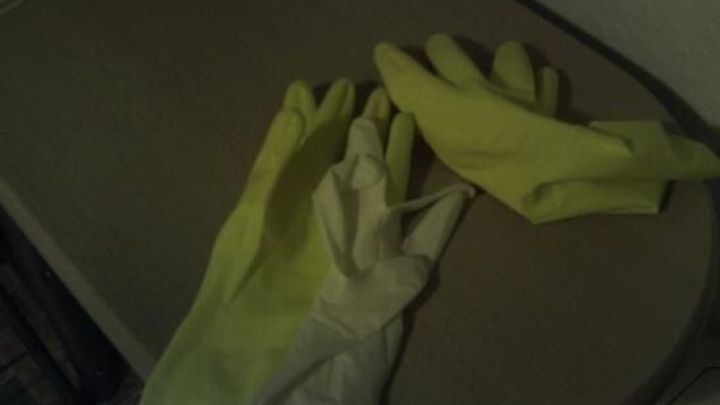 Zwei Handschuhe liegen auf einem Tisch: ein wei&szlig;er Latexhandschuh unter einem gr&uuml;nen Gummihandschuh.