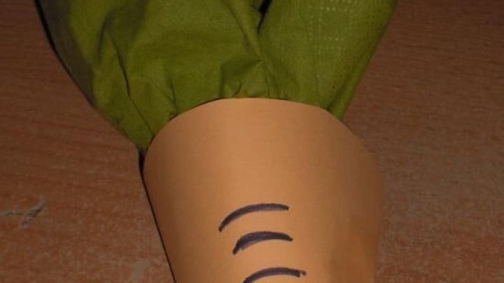 Ein orangefarbenes Serviettenformat in Form einer M&ouml;hre h&auml;lt gr&uuml;ne Serviettenbl&auml;tter, ideal f&uuml;r Ostern.