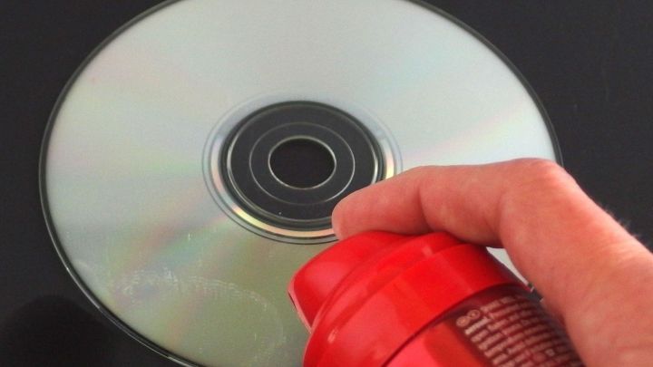 Ein Hand h&auml;lt eine rote Spr&uuml;hdose &uuml;ber eine gl&auml;nzende CD, w&auml;hrend Haarspray auf die CD aufspr&uuml;ht.