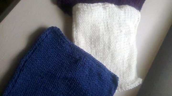 Bunte, gestrickte Quadrate einer molligen Patchworkdecke liegen auf einem Tisch und warten darauf, verbunden zu werden.