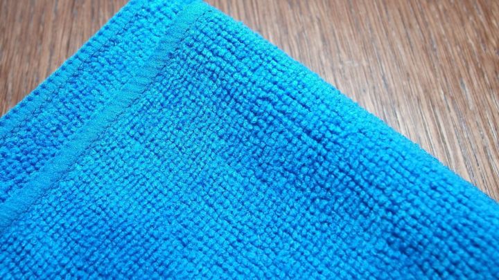 Ein Mikrofasertuch liegt auf einer Holzoberfl&auml;che, bereit, um Fenster effizient zu reinigen und Streifen zu vermeiden.