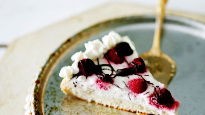 Ein St&uuml;ck Kuchen liegt auf einem silbernen Teller, w&auml;hrend ein goldener L&ouml;ffel daneben ruht. Fruchtige Leckereien sind sichtbar.