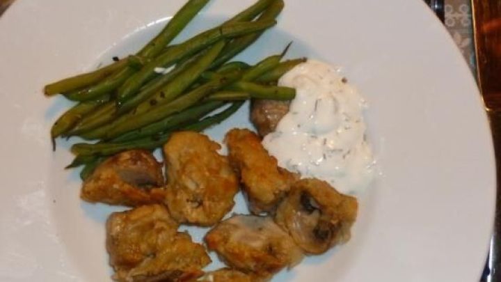 Knusprige Champignons im Backteig liegen auf einem Teller neben frischen gr&uuml;nen Bohnen und einer wei&szlig;en Dipsauce.