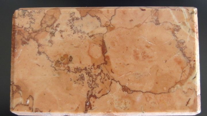 Ein rechteckiges Marmorobjekt liegt flach auf einer dunklen Unterlage und zeigt seine charakteristische, marmorierte Oberfl&auml;che.