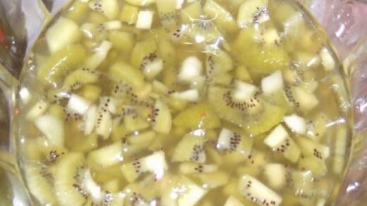 Eine Sch&uuml;ssel Kiwi-Bowle gef&uuml;llt mit geschnittenen Kiwi-St&uuml;cken in klarer Fl&uuml;ssigkeit, gl&auml;nzend im Licht.