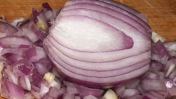 Eine geschnittene Zwiebel liegt auf einem Holzbrett, w&auml;hrend der l&auml;stige Zwiebelgeruch in der K&uuml;che verweilt.