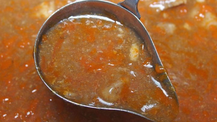 Ein silberner Sch&ouml;pfl&ouml;ffel nimmt Bratenso&szlig;e aus einem tiefen Topf, gef&uuml;llt mit w&uuml;rziger, dunkler So&szlig;e.