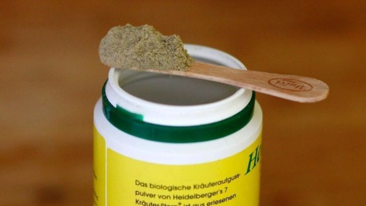 Ein Holzspatel steht auf einem ge&ouml;ffneten Beh&auml;lter mit Gew&uuml;rzpulver, das auf einem Holztisch platziert ist.