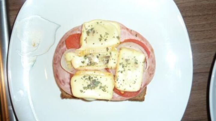 Ein herzhaft belegtes Brot mit Wurst, Tomaten und geschmolzenem K&auml;se, das auf einem wei&szlig;en Teller serviert wird.